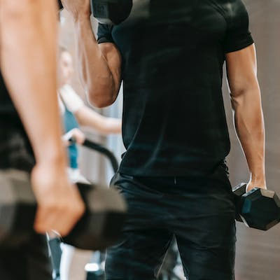 عکسی از یک بدنساز با عضلات پشت بزرگ و تعریف شده. در حال انجام حرکات بدنسازی و استفاده از ماشین های وزنه برای تقویت عضلات پشت و سرشانه ها است.